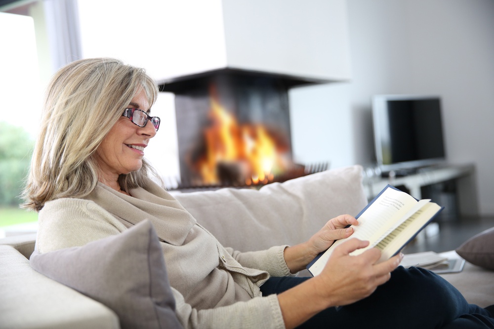 Senior woman reading book at home by fireplace